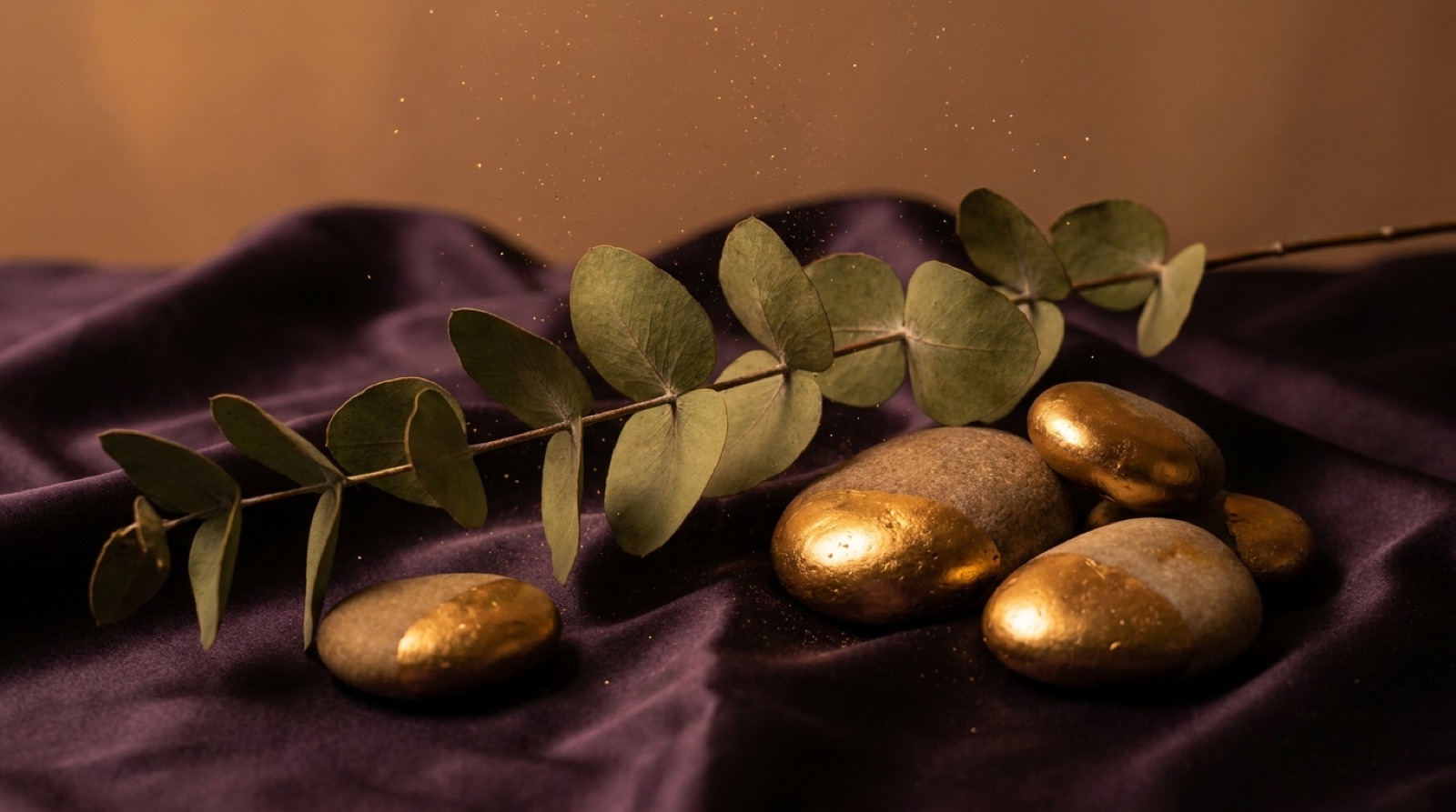 Eucalyptus branch and river stones dipped in gold resting on dark violet silk